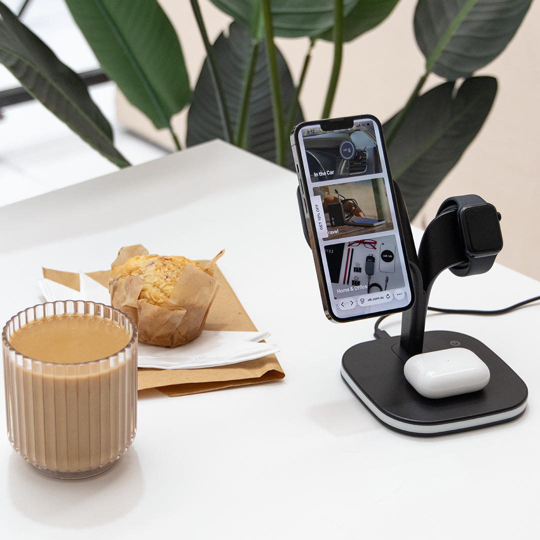Multi-device charging stand with phone, watch, and mouse on a desk with a cup of coffee and pastry.